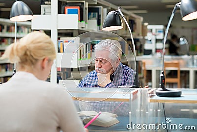 Senior man studying among young people in library