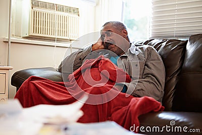 Senior Man Trying To Keep Warm Under Blanket At Home