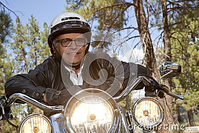 Senior man wearing helmet leaning on motorcycle handlebars in forest