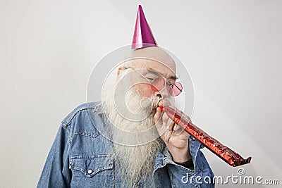 Senior man wearing party hat while blowing horn against gray background