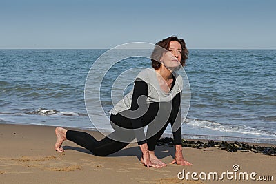 Senior woman doing yoga sun salutation on the beach