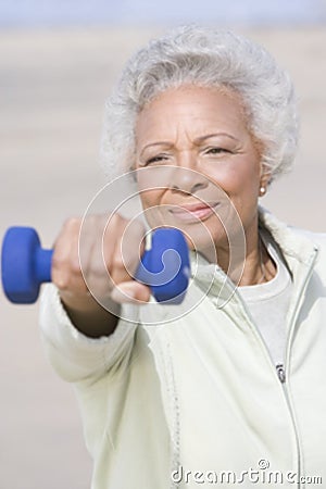 Senior Woman Exercising With Dumbbells At Beach