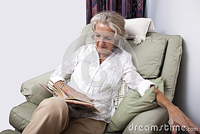 Senior woman reading book while relaxing on armchair at home