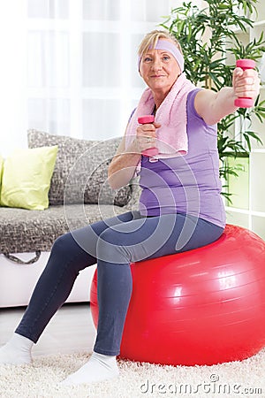 Senior woman sitting on gym ball, and exercise with weights at h