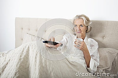Senior woman watching TV while having coffee in bed