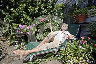 Senior woman with wineglass relaxing on lounge chair in garden