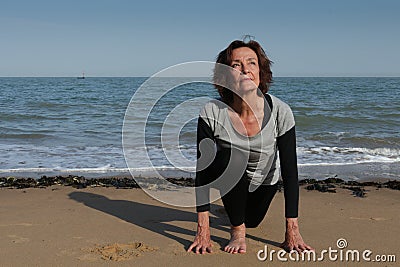 Mature woman yoga sun salutation on the beach