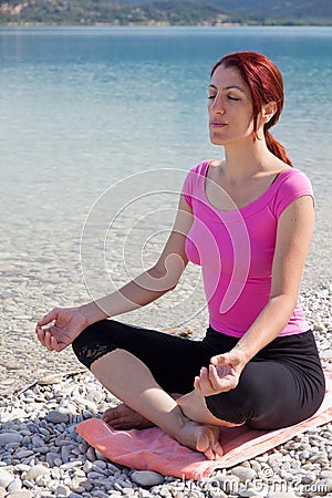 Serene woman meditating alongside a lake.