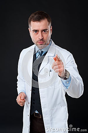 Serious male doctor pointing at camera on black background