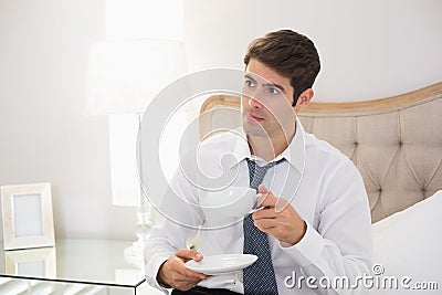 Serious well dressed man with a cup of tea in bed