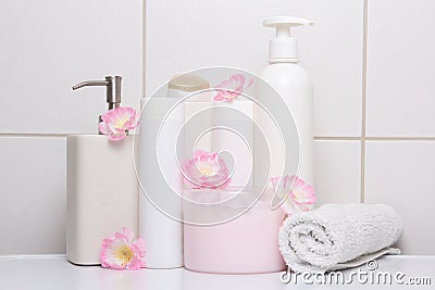 Set of white cosmetic bottles with pink flowers over tiled wall