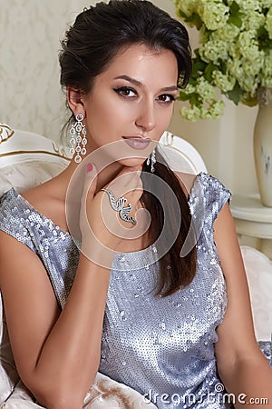 Sexy beautiful young brunette woman with evening make-up chic groomed wearing a short evening dress embroidered with silver