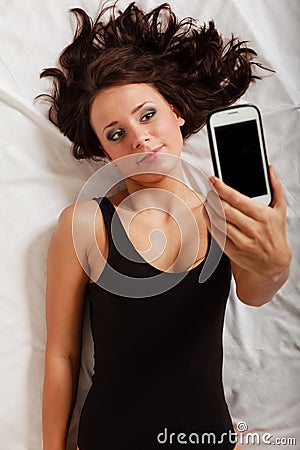 Sexy lazy girl lying with phone on bed in bedroom