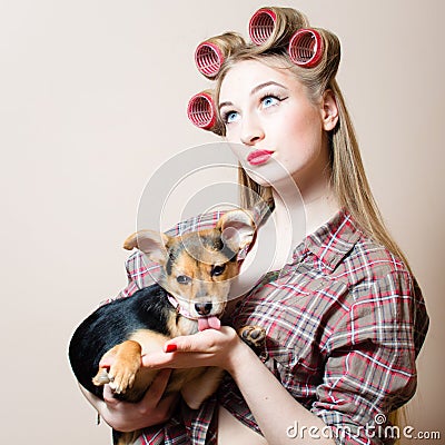 Sexy pinup girl with curlers on her head and a dog in her arms looking up on light copy space