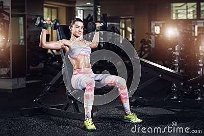 Sexy sporty woman exercising in gym with dumbbells