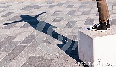 Shadow of a young woman with open arms projected on the pavement