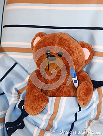 Sick teddy bear with thermometer in bed