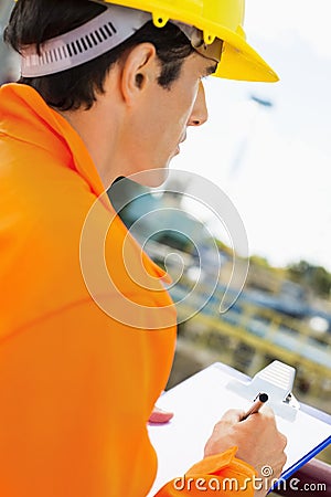 Side view of construction worker writing on clipboard at construction site