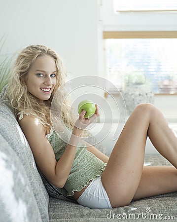 Side view portrait of young woman holding apple while sitting on sofa in house