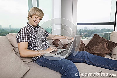 Side view of smiling mid-adult man using laptop on sofa at home