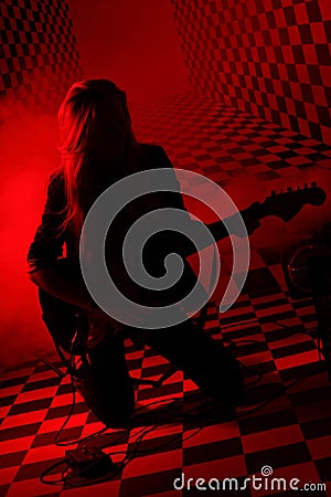 Silhouette of girl kneeling and playing electric guitar