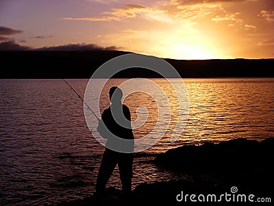 Silhouette of man sea fishing at sunset