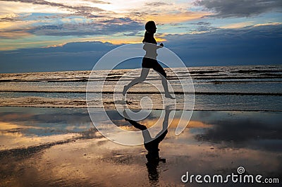 Silhouette of woman jogger running on sunset beach with reflection