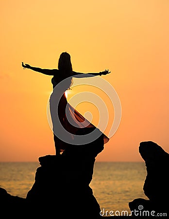 A silhouette of a young girl on rock at sunset 3