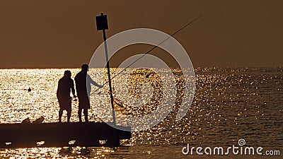 Silhouettes of fishermen on sea sunset background