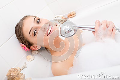 Singing spa: Beautiful happy smiling girl sexy woman lying relaxing in the bath with foam holding shower in the hands having fun