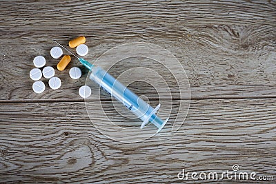 Single syringe and pills on wooden board