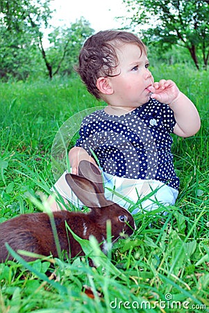 Sitting on the grass a little girl, and by her black rabbit.