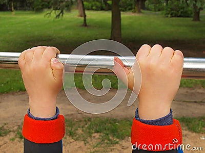 Small children hands are hanging on steel horizontal bar. Children playground