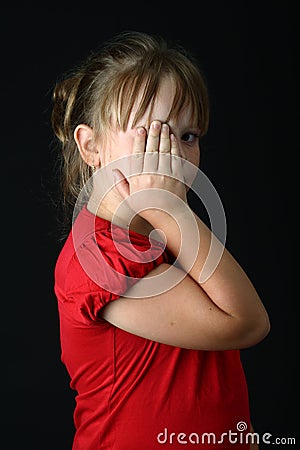 Small girl covering one eye with her hand on black