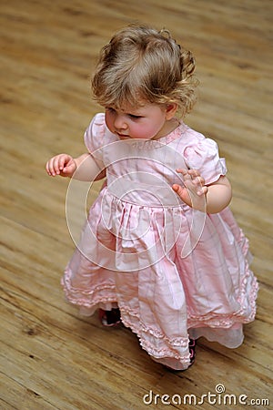 Small girl standing in pink dress on wooden floor