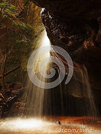 Small waterfall on small mountain stream, mossy sandstone block and water is jumping down into small pool. Water streams with sun.