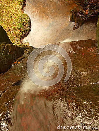 Small waterfall on small mountain stream, mossy sandstone block and water is jumping down into small pool. Water streams with sun.