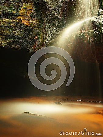 Small waterfall on small mountain stream, mossy sandstone block and water is jumping down into small pool. Water streams with sun.