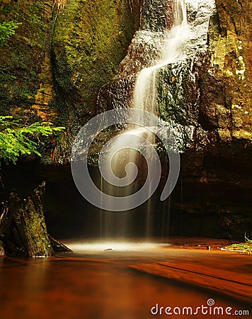 Small waterfall on small mountain stream, mossy sandstone block and water is jumping down into small pool. Water streams with sun.