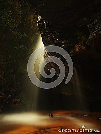 Small waterfall on small mountain stream, mossy sandstone block and water is jumping down into small pool. Water streams with sun.