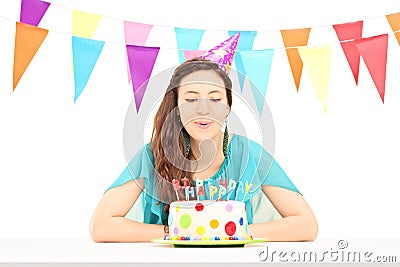 A smiling birthday female with a party hat blowing the candles o