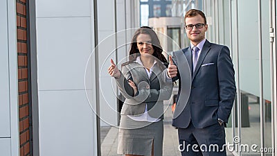 A smiling business man and woman are posing. Thumb up.
