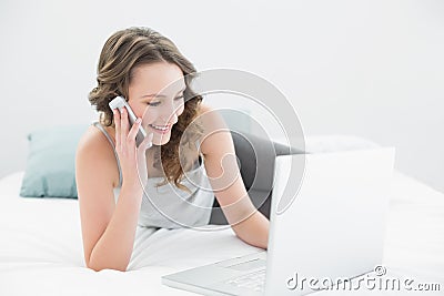 Smiling casual woman using cellphone and laptop in bed