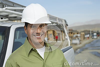 Smiling Construction Worker In Hardhat By Truck On Site