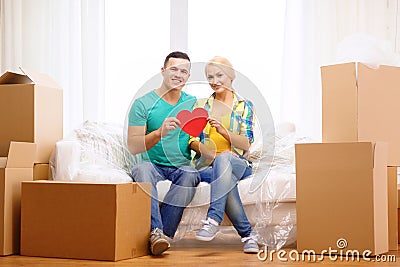 Smiling couple with red heart on sofa in new home