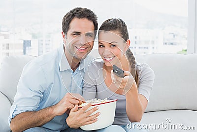 Smiling couple watching tv on the couch with bowl of popcorn