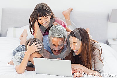 Smiling family lying on bed using their laptop