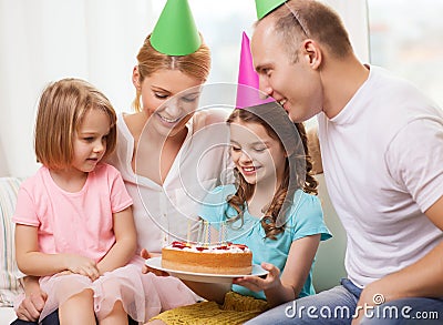 Smiling family with two kids in hats with cake