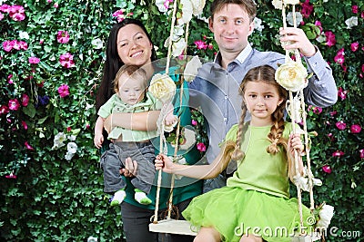 Smiling father, mother with baby and little daughter on swing