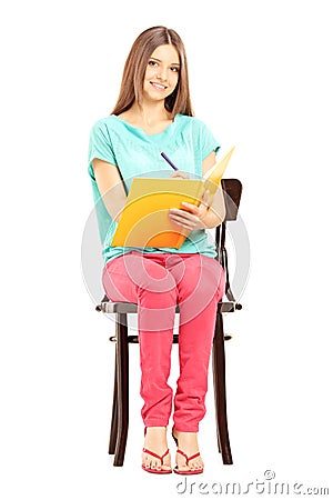 Smiling female student sitting on a chair and writing notes